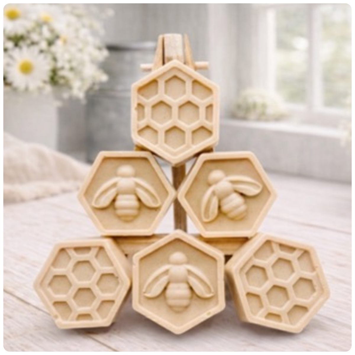 A handmade vegan soap gift set featuring six hexagonal bars stacked in a pyramid on a small wooden easel; some bars show a honeybee relief and others a honeycomb pattern