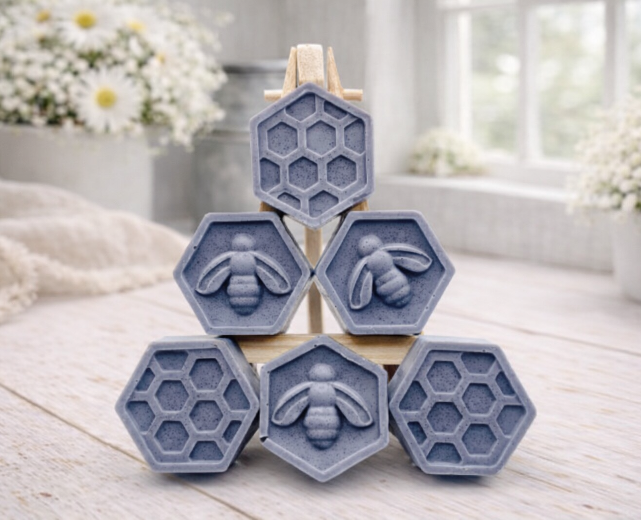A handmade vegan soap gift set featuring six hexagonal bars stacked in a pyramid on a small wooden easel; some bars show a honeybee relief and others a honeycomb pattern