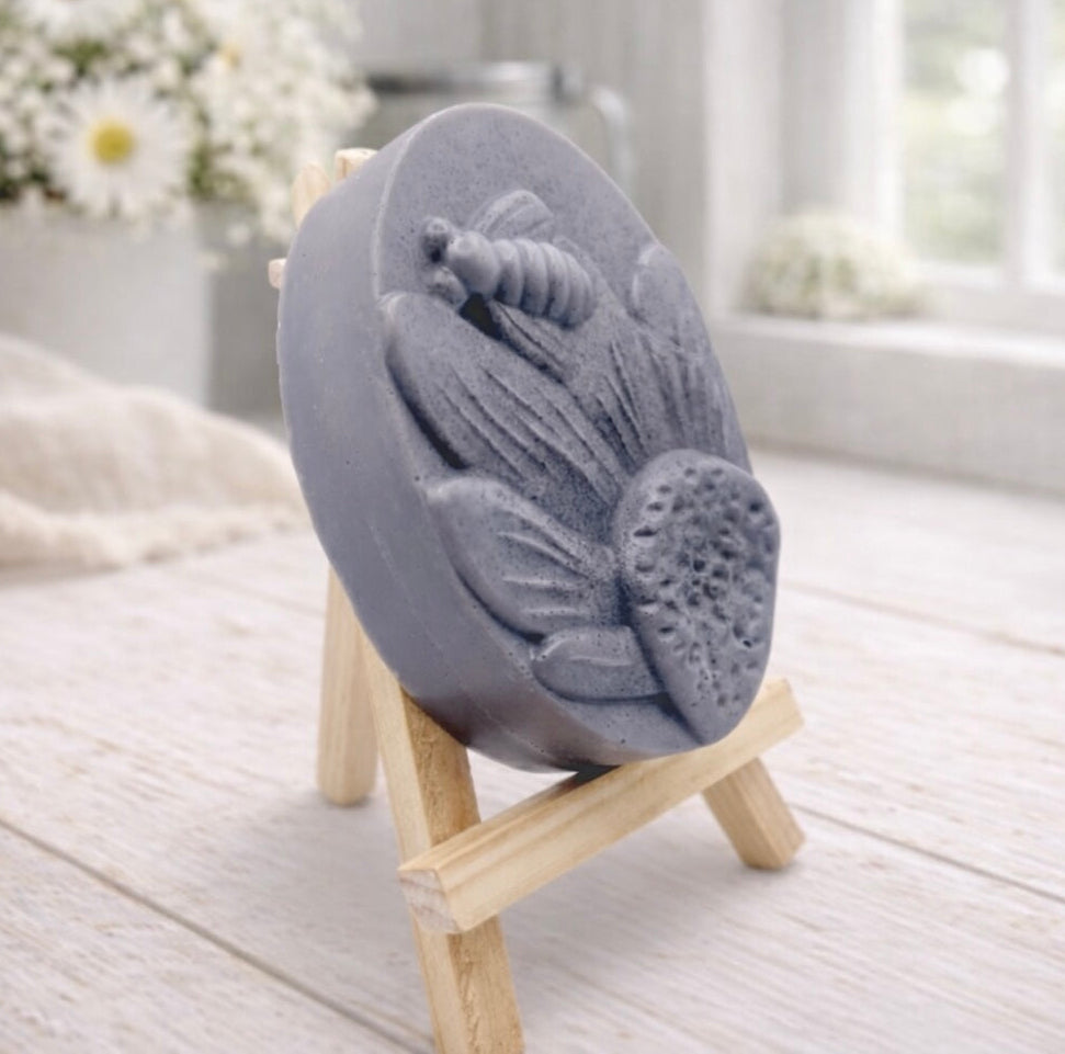 handmade vegan soap gift featuring a detailed honey bee landing on a large sunflower, displayed on a wooden easel against a whimsical farmhouse decor background.