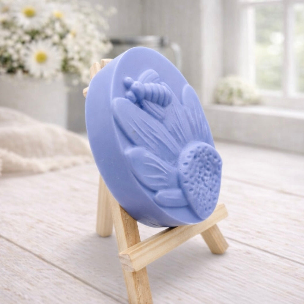 handmade vegan soap gift featuring a detailed honey bee landing on a large sunflower, displayed on a wooden easel against a whimsical farmhouse decor background.