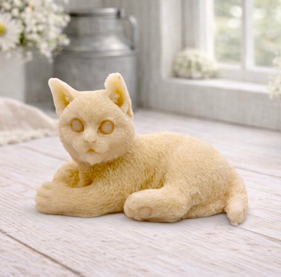 A highly detailed handmade vegan soap sculpted in the shape of a sitting cat with its tail curled around its paws, featuring realistic fur texture and a sweet facial expression, displayed on a light wooden surface.