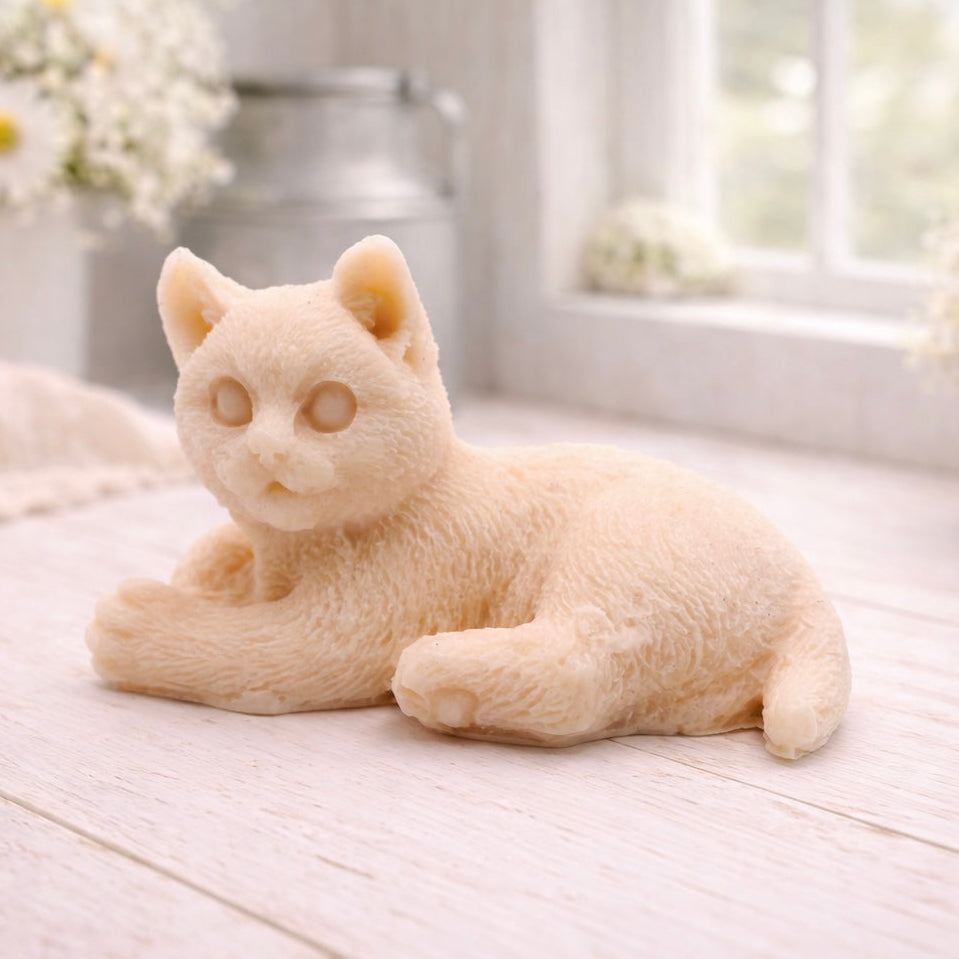 A highly detailed handmade vegan soap sculpted in the shape of a sitting cat with its tail curled around its paws, featuring realistic fur texture and a sweet facial expression, displayed on a light wooden surface.