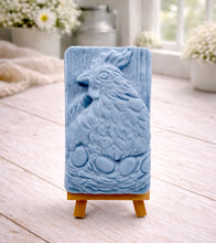 Load image into Gallery viewer, A rectangular handmade vegan soap in a natural colour, featuring a highly detailed relief carving of a broody hen chicken sitting on a nest of eggs, displayed upright on a light wooden surface.
