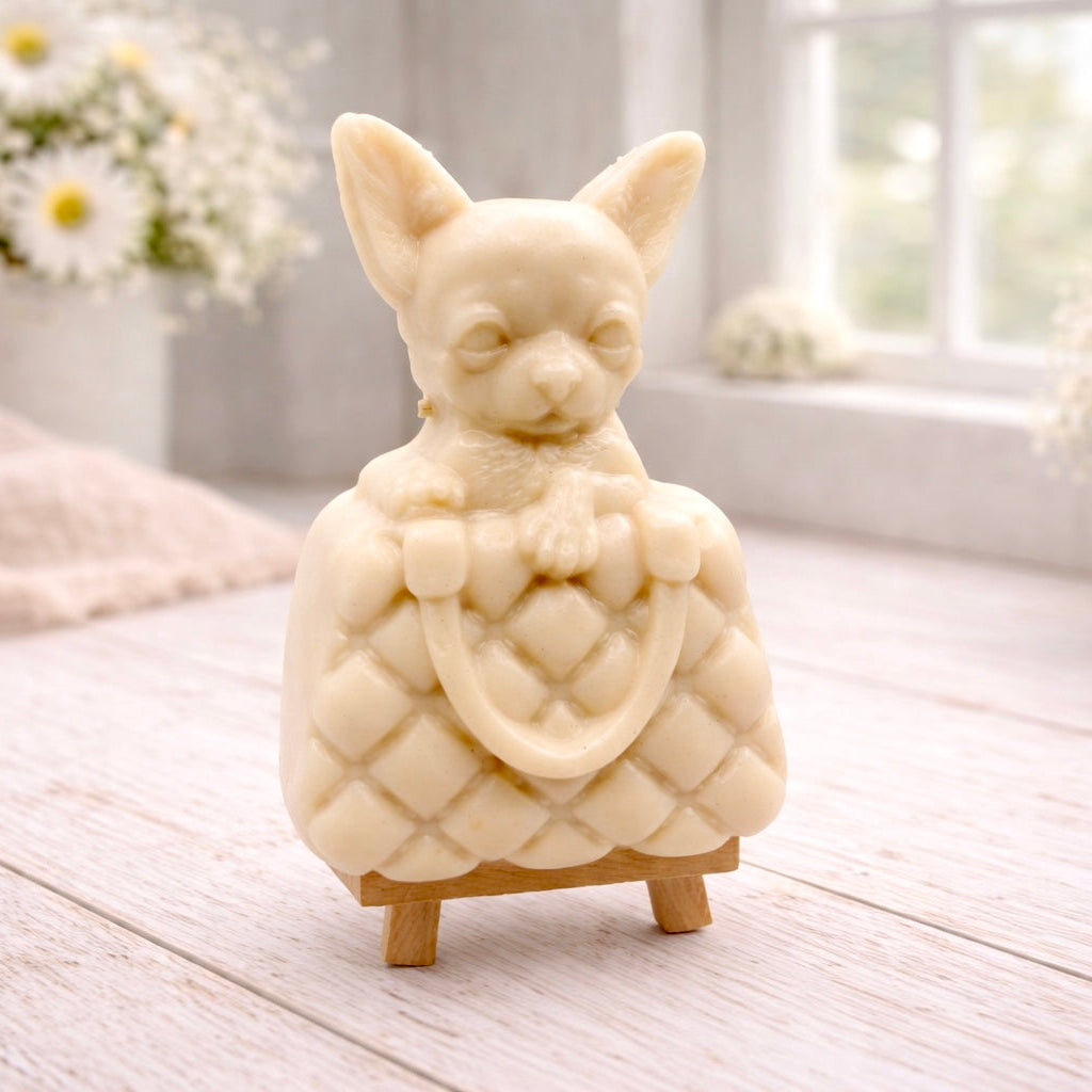 A highly detailed handmade vegan soap in a speckled grey marble finish, sculpted as a small chihuahua puppy with large ears peeking out from inside a quilted designer-style handbag, displayed on a miniature wooden easel.