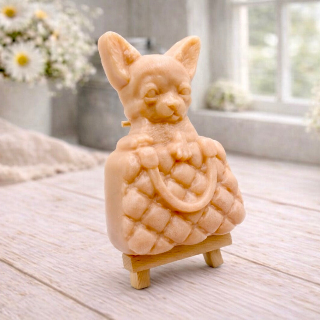 A highly detailed handmade vegan soap in a speckled grey marble finish, sculpted as a small chihuahua puppy with large ears peeking out from inside a quilted designer-style handbag, displayed on a miniature wooden easel.