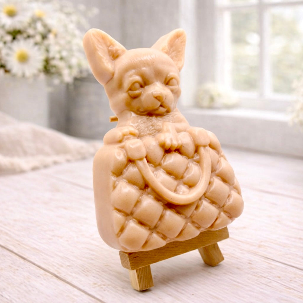 A highly detailed handmade vegan soap in a speckled grey marble finish, sculpted as a small chihuahua puppy with large ears peeking out from inside a quilted designer-style handbag, displayed on a miniature wooden easel.