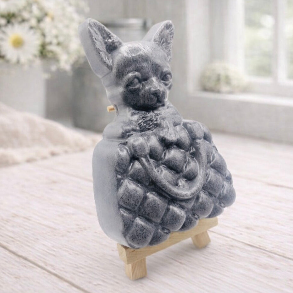A highly detailed handmade vegan soap in a speckled grey marble finish, sculpted as a small chihuahua puppy with large ears peeking out from inside a quilted designer-style handbag, displayed on a miniature wooden easel.