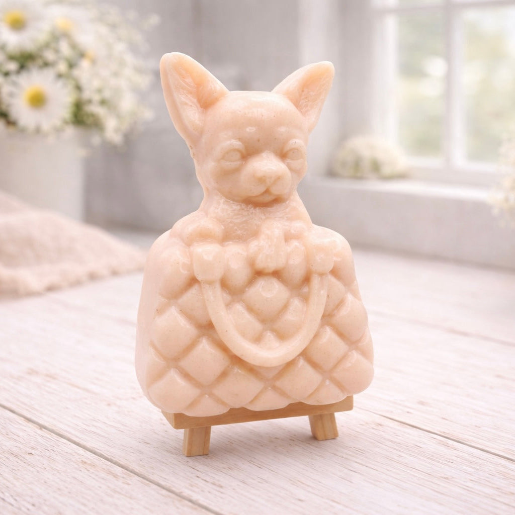 A highly detailed handmade vegan soap in a speckled grey marble finish, sculpted as a small chihuahua puppy with large ears peeking out from inside a quilted designer-style handbag, displayed on a miniature wooden easel.