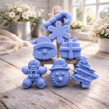 Load image into Gallery viewer, A collection of six handmade vegan Christmas soaps featuring a candy cane, snowflake, Santa Claus face, wrapped gift box, gingerbread man, snowman, and a decorated Christmas tree, arranged in a pyramid on a wooden stand.

