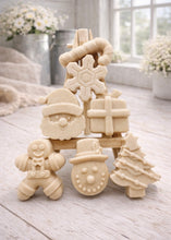 Load image into Gallery viewer, A collection of six handmade vegan Christmas soaps featuring a candy cane, snowflake, Santa Claus face, wrapped gift box, gingerbread man, snowman, and a decorated Christmas tree, arranged in a pyramid on a wooden stand.
