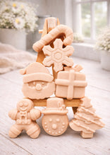 Load image into Gallery viewer, A collection of six handmade vegan Christmas soaps featuring a candy cane, snowflake, Santa Claus face, wrapped gift box, gingerbread man, snowman, and a decorated Christmas tree, arranged in a pyramid on a wooden stand.
