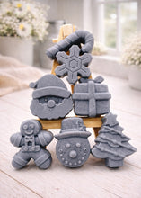 Load image into Gallery viewer, A collection of six handmade vegan Christmas soaps featuring a candy cane, snowflake, Santa Claus face, wrapped gift box, gingerbread man, snowman, and a decorated Christmas tree, arranged in a pyramid on a wooden stand.

