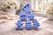 Load image into Gallery viewer, A collection of six handmade vegan Christmas soaps featuring a candy cane, snowflake, Santa Claus face, wrapped gift box, gingerbread man, snowman, and a decorated Christmas tree, arranged in a pyramid on a wooden stand.

