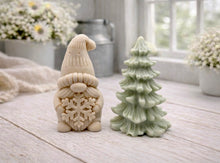 Load image into Gallery viewer, A pair of handmade vegan soaps featuring a Christmas gonk (gnome) with a textured hat holding a large snowflake, standing next to a pale mint-green 3D Christmas tree with layered, snow-dusted branches, displayed in a bright farmhouse setting.
