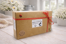 Load image into Gallery viewer, Kraft paper box with red ribbon on a wooden surface with blurred flowers in the background
