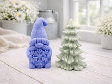Load image into Gallery viewer, A pair of handmade vegan soaps featuring a Christmas gonk (gnome) with a textured hat holding a large snowflake, standing next to a pale mint-green 3D Christmas tree with layered, snow-dusted branches, displayed in a bright farmhouse setting.

