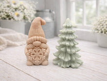 Load image into Gallery viewer, A pair of handmade vegan soaps featuring a Christmas gonk (gnome) with a textured hat holding a large snowflake, standing next to a pale mint-green 3D Christmas tree with layered, snow-dusted branches, displayed in a bright farmhouse setting.

