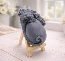 Load image into Gallery viewer, A 3D handmade vegan soap in a charcoal-grey tone, sculpted as a large prehistoric egg with a small dinosaur or dragon clinging to the top, featuring detailed scales and a curled tail, displayed on a miniature wooden easel.
