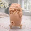 A 3D handmade vegan soap in a charcoal-grey tone, sculpted as a large prehistoric egg with a small dinosaur or dragon clinging to the top, featuring detailed scales and a curled tail, displayed on a miniature wooden easel.