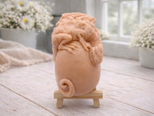 Load image into Gallery viewer, A 3D handmade vegan soap in a charcoal-grey tone, sculpted as a large prehistoric egg with a small dinosaur or dragon clinging to the top, featuring detailed scales and a curled tail, displayed on a miniature wooden easel.
