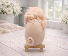 Load image into Gallery viewer, A 3D handmade vegan soap in a charcoal-grey tone, sculpted as a large prehistoric egg with a small dinosaur or dragon clinging to the top, featuring detailed scales and a curled tail, displayed on a miniature wooden easel.
