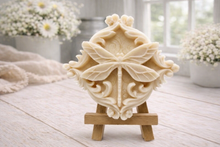 Load image into Gallery viewer, A beautiful handmade vegan soap in a natural tone, featuring a highly detailed relief of a dragonfly with delicate, outspread wings and a textured body, displayed on a miniature wooden easel against a soft farmhouse background.
