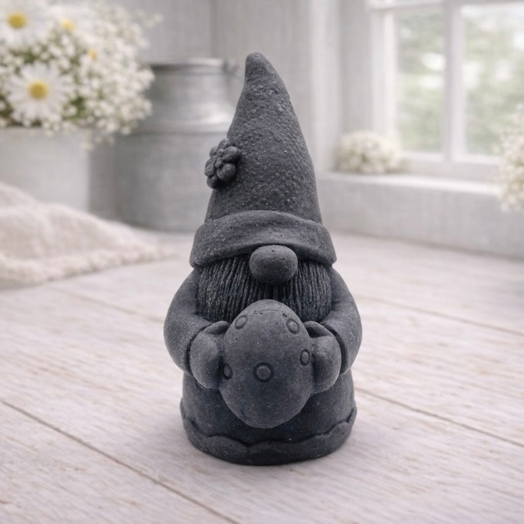 A detailed handmade vegan soap gift,  sculpted as a whimsical Easter gnome (gonk) wearing a tall pointed hat with a flower detail, holding a large patterned Easter egg.