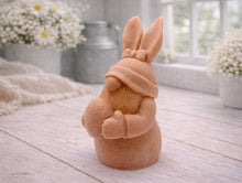 Load image into Gallery viewer, A detailed handmade vegan soap in a natural colour, sculpted as a whimsical Easter gnome (gonk) with long rabbit ears and a bow on its hat, holding a patterned Easter egg, displayed on a light wooden surface. Easter gift 
