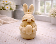 Load image into Gallery viewer, A detailed handmade vegan soap in a natural colour, sculpted as a whimsical Easter gnome (gonk) with long rabbit ears and a bow on its hat, holding a patterned Easter egg, displayed on a light wooden surface. Easter gift 
