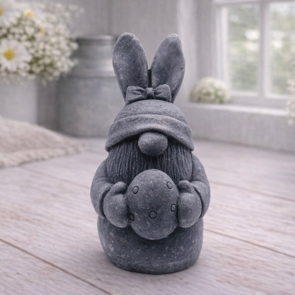 A detailed handmade vegan soap in a natural colour, sculpted as a whimsical Easter gnome (gonk) with long rabbit ears and a bow on its hat, holding a patterned Easter egg, displayed on a light wooden surface. Easter gift 