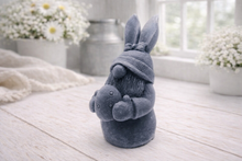 Load image into Gallery viewer, A detailed handmade vegan soap in a natural colour, sculpted as a whimsical Easter gnome (gonk) with long rabbit ears and a bow on its hat, holding a patterned Easter egg, displayed on a light wooden surface.
