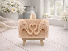 Load image into Gallery viewer, A rectangular handmade vegan soap  featuring a detailed relief of two elephants facing each other with their trunks entwined to form a heart shape, displayed on a miniature wooden easel.
