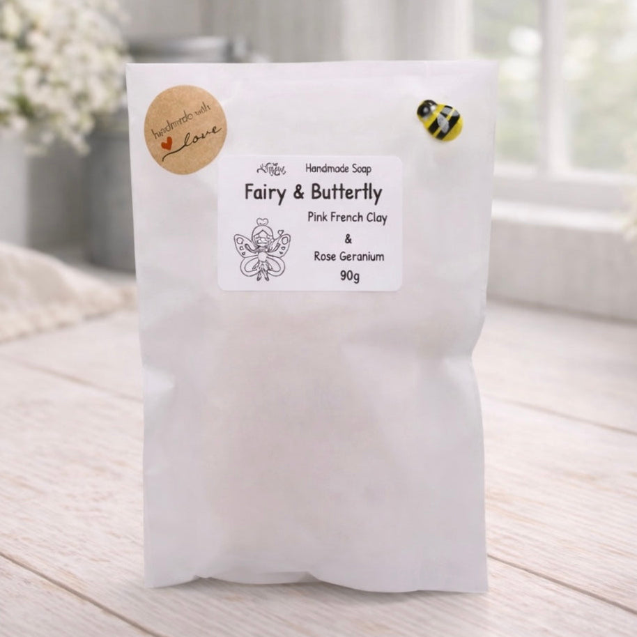 White soap packaging with a label on a wooden surface, flowers in the background