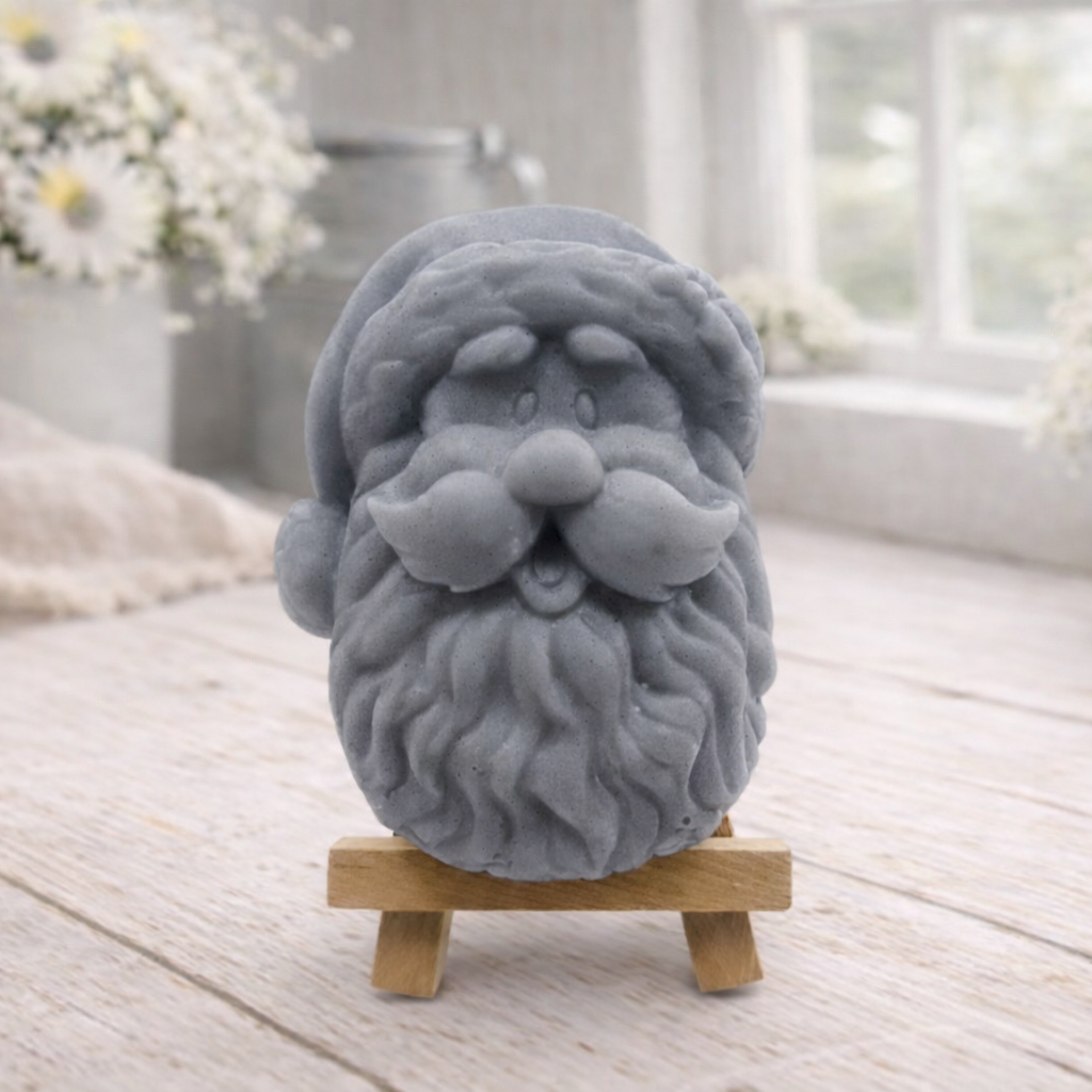 handmade vegan soap sculpted in the shape of Father Christmas's head, featuring a detailed curly beard, a jolly moustache, and a classic Santa hat, displayed on a miniature wooden easel in a bright farmhouse setting.