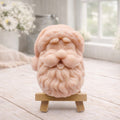 handmade vegan soap sculpted in the shape of Father Christmas's head, featuring a detailed curly beard, a jolly moustache, and a classic Santa hat, displayed on a miniature wooden easel in a bright farmhouse setting.