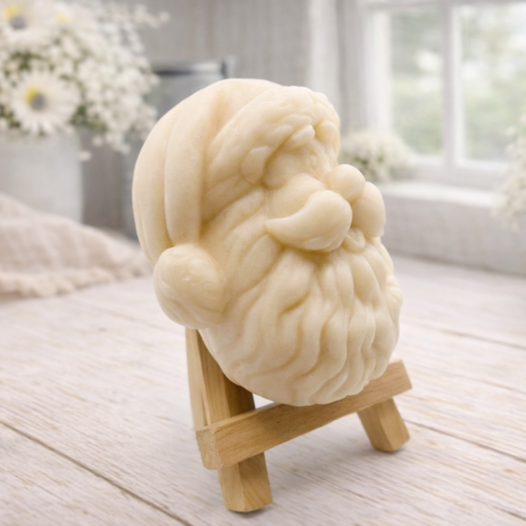 handmade vegan soap sculpted in the shape of Father Christmas's head, featuring a detailed curly beard, a jolly moustache, and a classic Santa hat, displayed on a miniature wooden easel in a bright farmhouse setting.