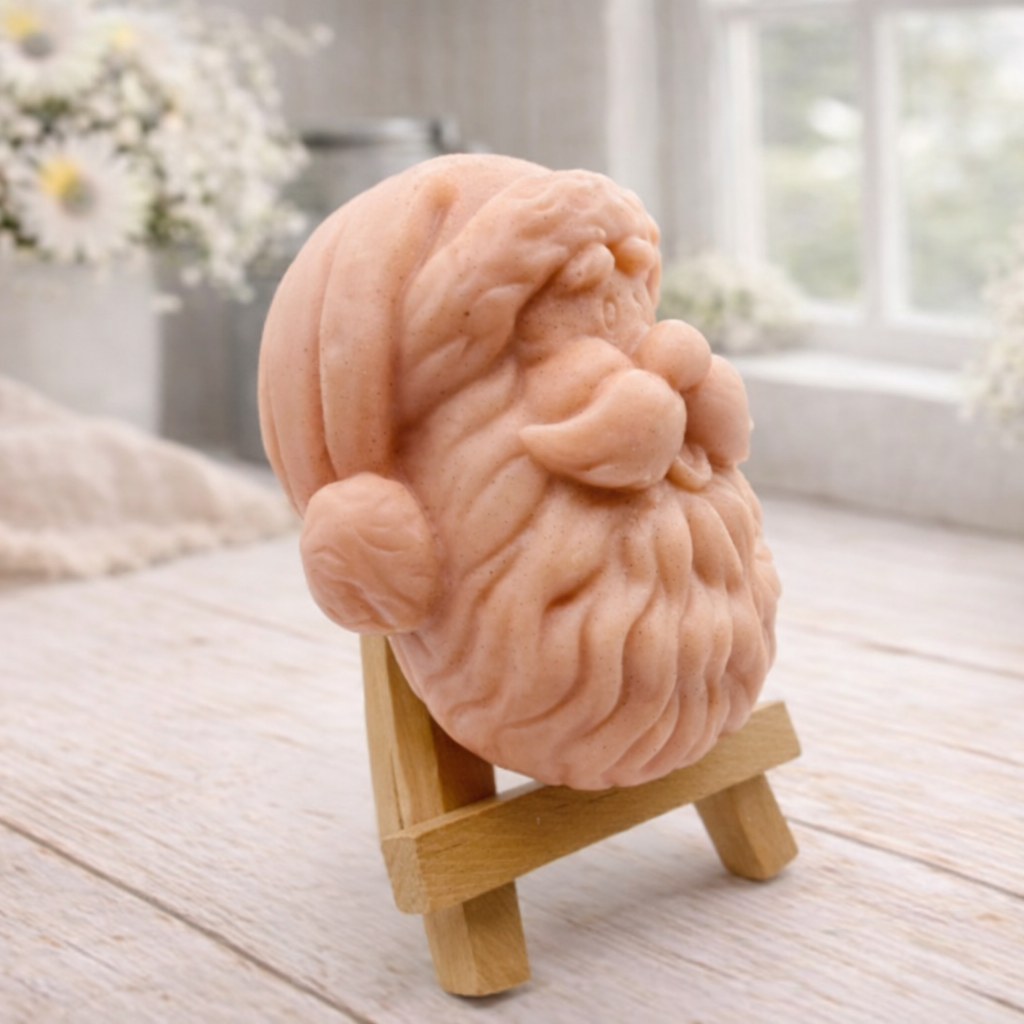 handmade vegan soap sculpted in the shape of Father Christmas's head, featuring a detailed curly beard, a jolly moustache, and a classic Santa hat, displayed on a miniature wooden easel in a bright farmhouse setting.