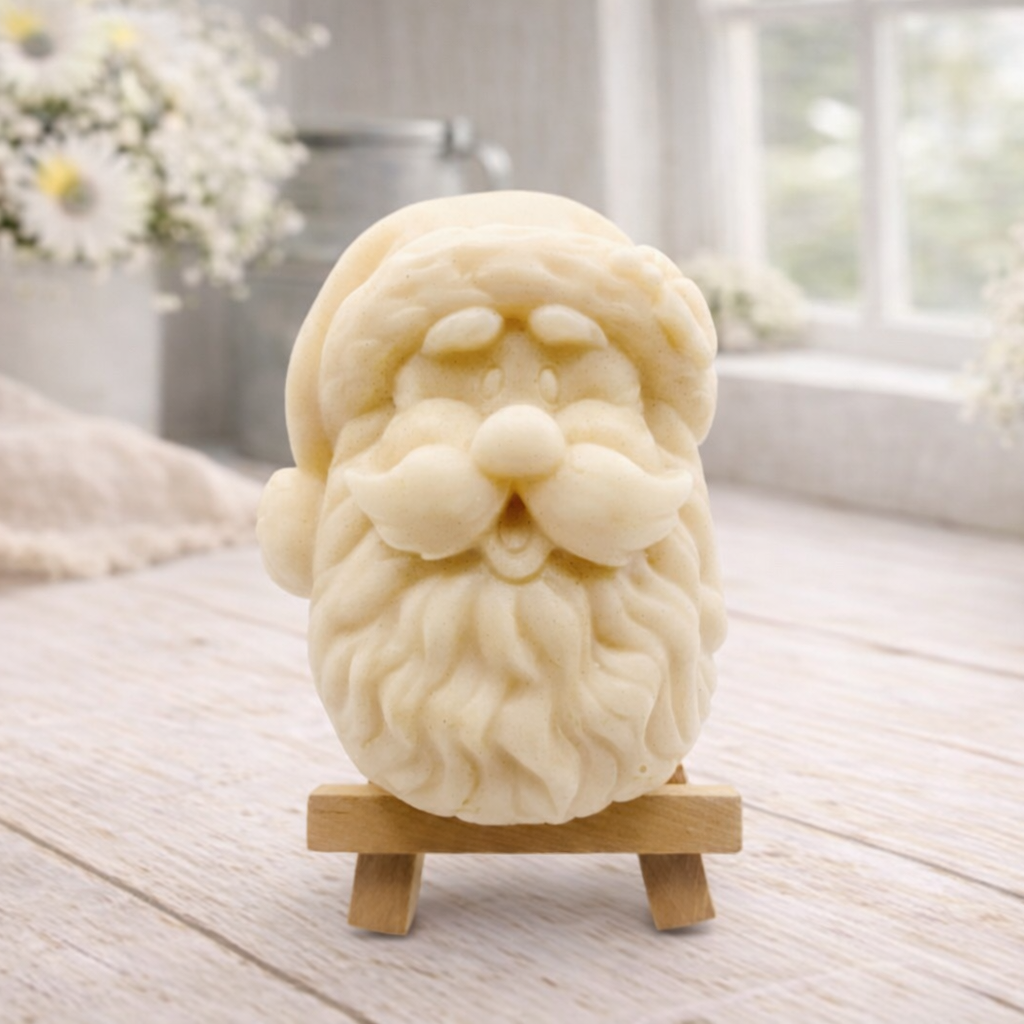 handmade vegan soap sculpted in the shape of Father Christmas's head, featuring a detailed curly beard, a jolly moustache, and a classic Santa hat, displayed on a miniature wooden easel in a bright farmhouse setting.