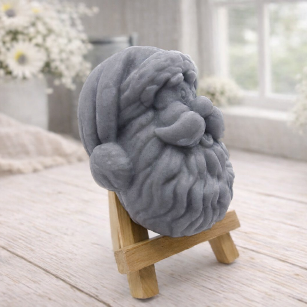 handmade vegan soap sculpted in the shape of Father Christmas's head, featuring a detailed curly beard, a jolly moustache, and a classic Santa hat, displayed on a miniature wooden easel in a bright farmhouse setting.