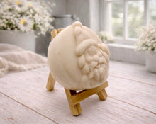 Load image into Gallery viewer, A circular handmade vegan soap featuring a detailed high-relief carving of a jolly Father Christmas waving, with a textured beard and a classic Santa hat, displayed on a miniature wooden easel.
