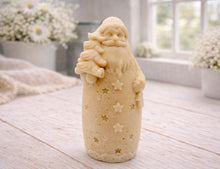 Load image into Gallery viewer, handmade vegan soap sculpted into a tall figure of Father Christmas wearing star-patterned robes, holding a small Christmas tree in one arm and a lantern in the other, set in a bright farmhouse window.
