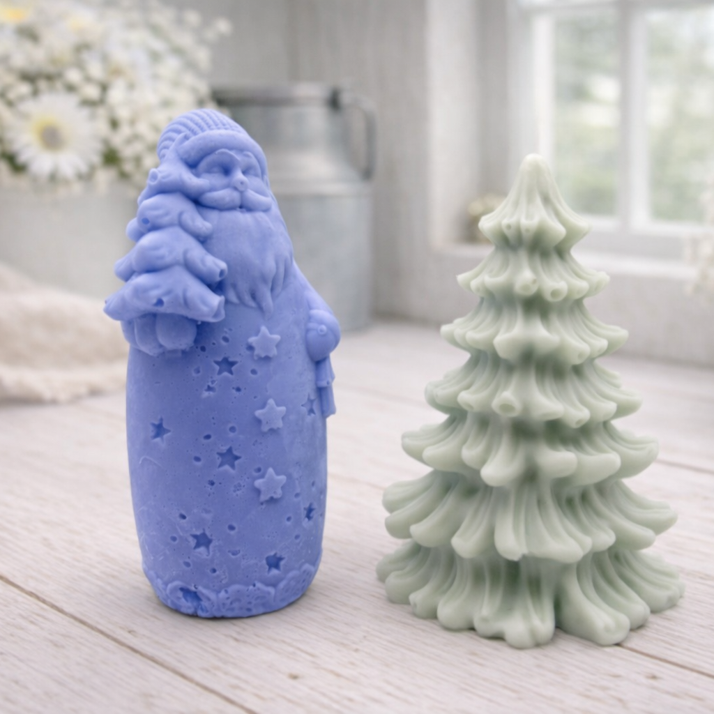 Blue Santa Claus and green Christmas tree-shaped vegan soap gift set on a wooden surface with white flowers in the background.