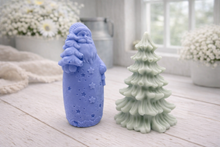 Load image into Gallery viewer, Blue Santa Claus and green Christmas tree-shaped vegan soap gift set on a wooden surface with white flowers in the background.
