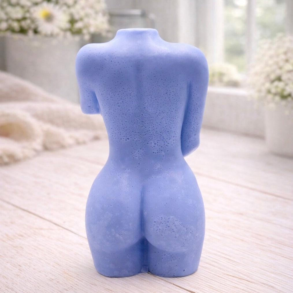 A 3D handmade vegan soap sculpted into a detailed female torso with soft, realistic curves and defined musculature and displayed in a bright farmhouse setting.