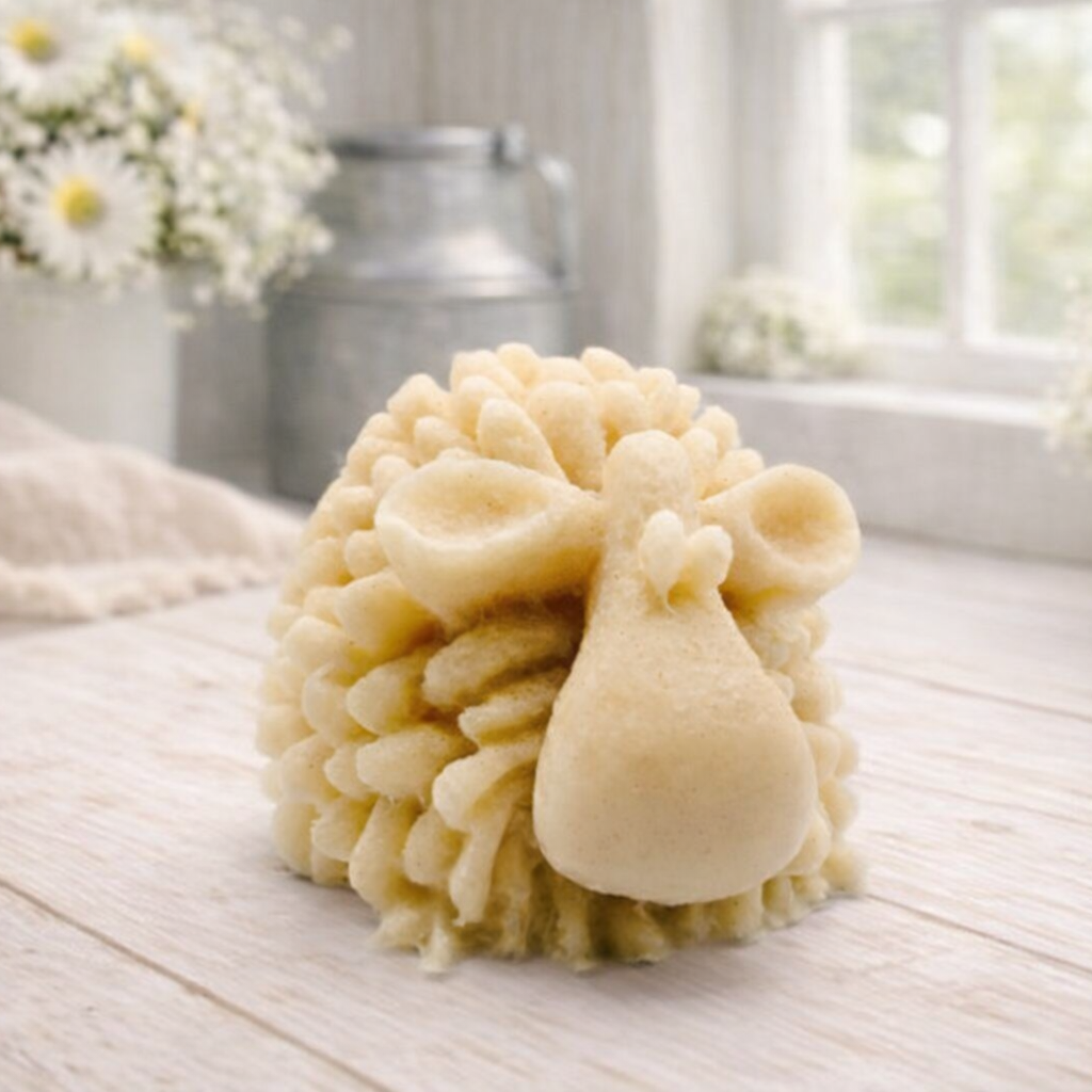 A highly detailed handmade vegan soap sculpted in the shape of a fluffy sheep with thick, textured wool and a smooth face, displayed on a light wooden surface in a farmhouse-style setting.