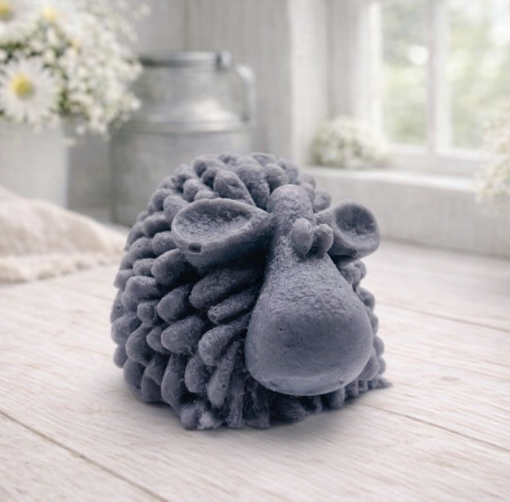 A highly detailed handmade vegan soap sculpted in the shape of a fluffy sheep with thick, textured wool and a smooth face, displayed on a light wooden surface in a farmhouse-style setting.
