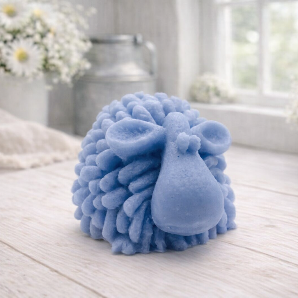 A highly detailed handmade vegan soap sculpted in the shape of a fluffy sheep with thick, textured wool and a smooth face, displayed on a light wooden surface in a farmhouse-style setting.