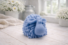 Load image into Gallery viewer, A highly detailed handmade vegan soap sculpted in the shape of a fluffy sheep with thick, textured wool and a smooth face, displayed on a light wooden surface in a farmhouse-style setting.
