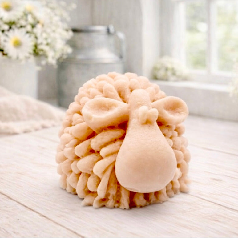 A highly detailed handmade vegan soap sculpted in the shape of a fluffy sheep with thick, textured wool and a smooth face, displayed on a light wooden surface in a farmhouse-style setting.