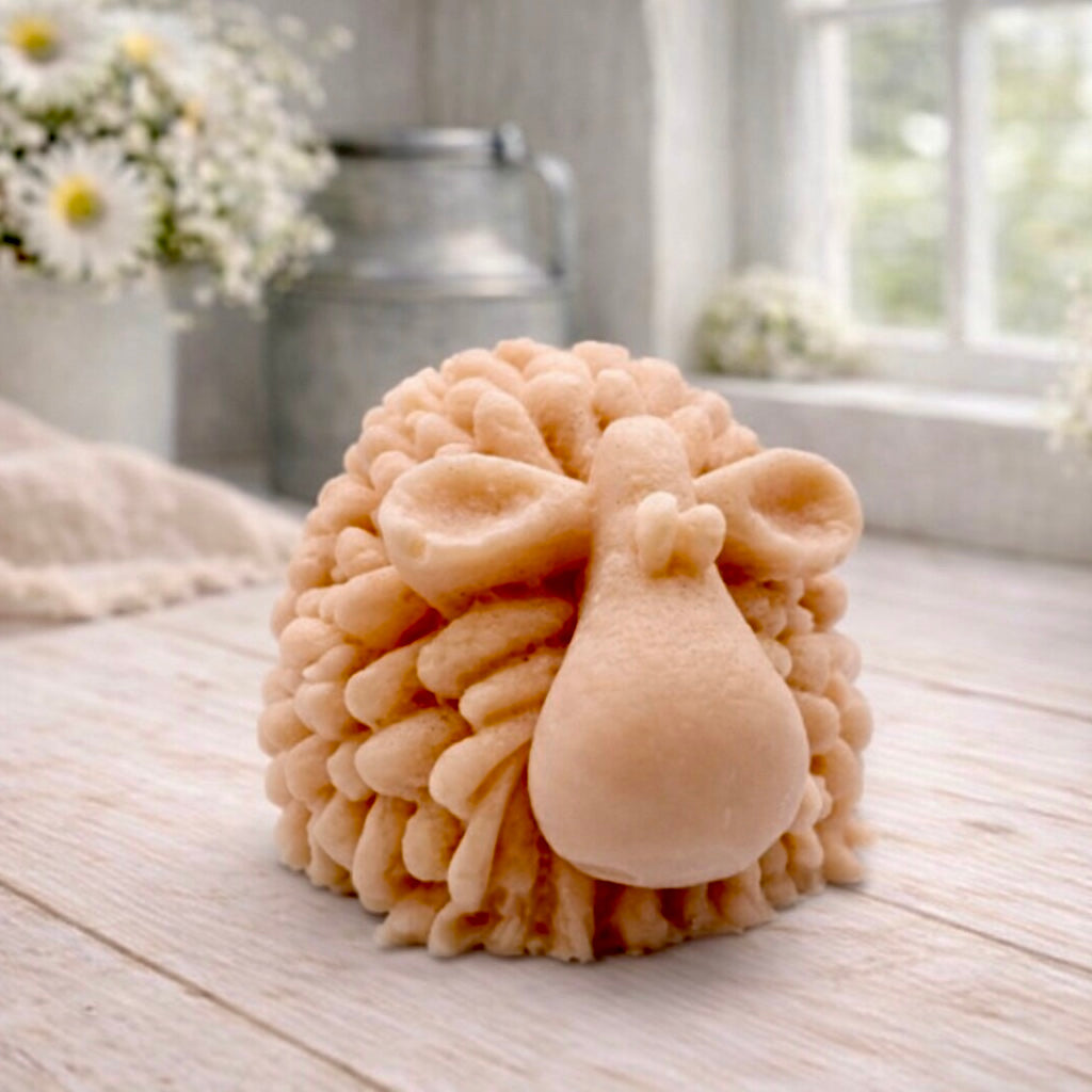 A highly detailed handmade vegan soap sculpted in the shape of a fluffy sheep with thick, textured wool and a smooth face, displayed on a light wooden surface in a farmhouse-style setting.
